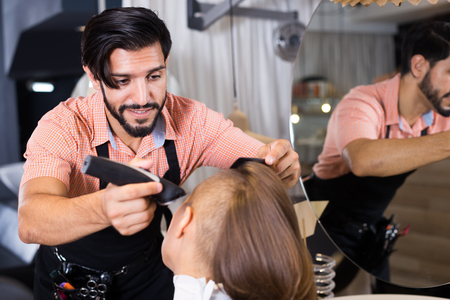Positive sexy adult hairdresser working with hair clipper with womanの写真素材