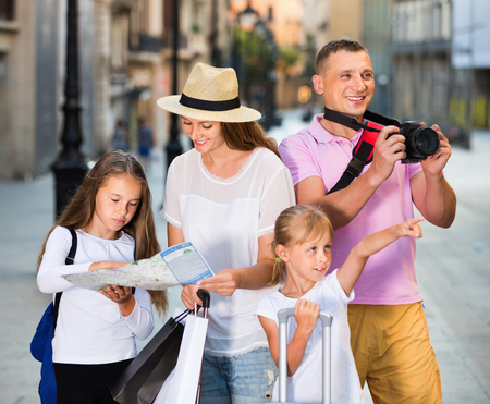 Happy cheerful  tourist family using map and taking photo of city while strolling with camera and phoneの写真素材