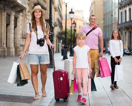 Happy swiss traveling family of four strolling with luggage along European city streetの写真素材
