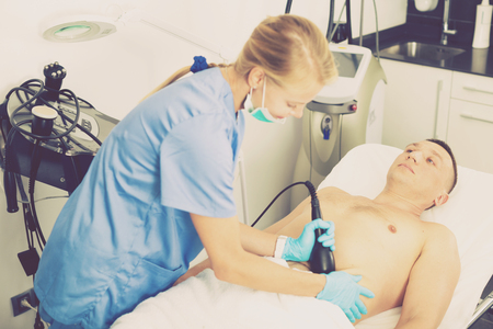 Woman doctor is doing vacuum massage procedure on belly of adult client in clinic.の写真素材