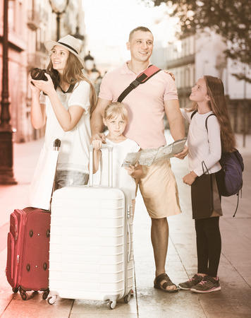 Positive tourist family with kids using map and  making amateur photo of sights in Europe cityの写真素材