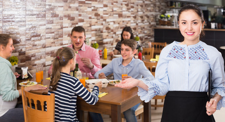 Professional waitress holding tray with dishes meeting visitors in cafeの写真素材