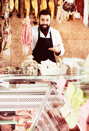 Young male seller offering delicious sausages in butchers shopの写真素材