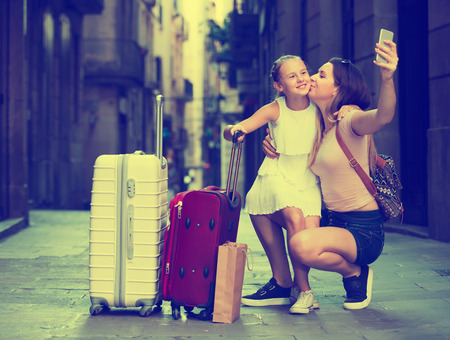 Smiling woman with little girl making selfie on European city during joint vacationの写真素材