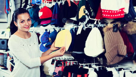 Happy adult woman choosing new knit cap in sports storeの写真素材
