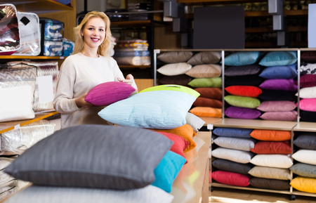 happy american female shop assistant demonstrating assortment of home textilesの写真素材