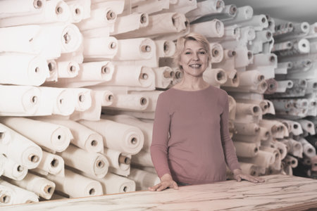 Mature woman buyer is showing bought home textiles in textile shop.