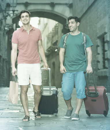 Two men friends walking together with baggage in Barcelonaの写真素材