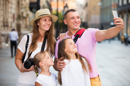 Cheerful tourist family of four strolling on city streets and taking selfieの写真素材