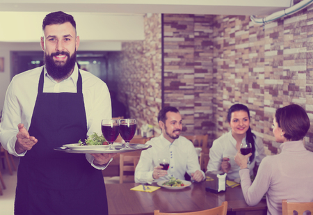 smiling waiter serving dear restaurant guests at tableの写真素材