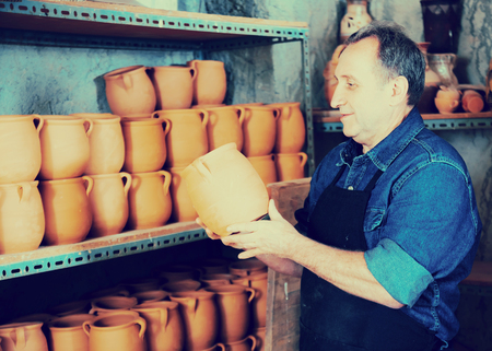 Portrait of smiling elderly man with ceramic crocks  at pottery workshopの写真素材