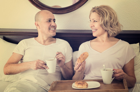 Mature adults posing with coffee and croissant for breakfastの写真素材