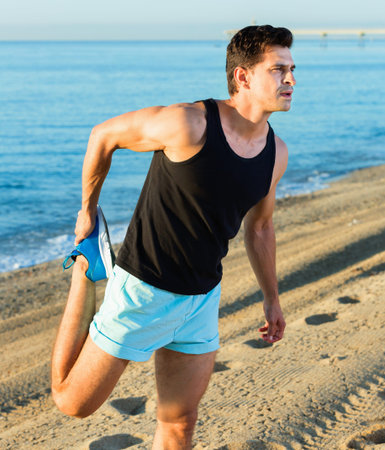 Physically fit cheerful positive  man doing stretching exercises on morning beach