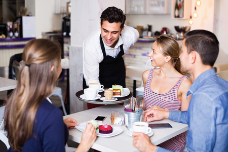 Smiling waiter showing hospitality and serving visitors in cozy coffeehouseの写真素材
