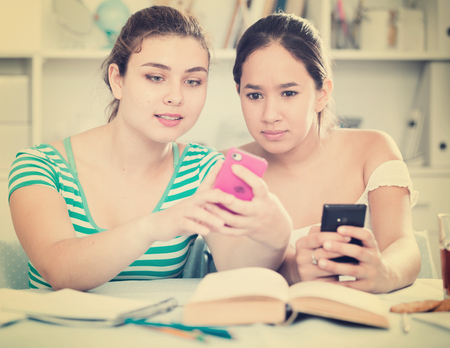 Cheerful teens girls spending time together at home, chatting on phonesの写真素材