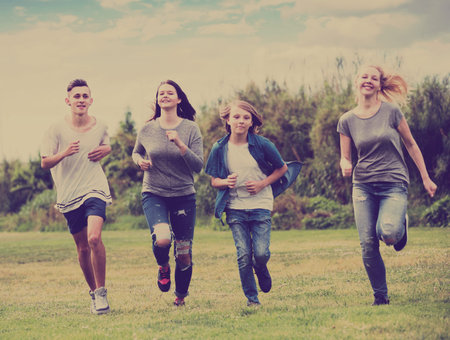 Two active girl and two boys teenagers friends running on meadow outdoors