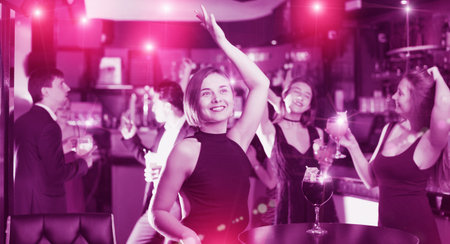 Positive adult females and males celebrating corporate in the bar at night