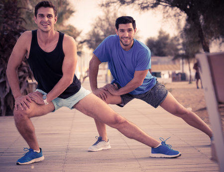 Portrait of sportsmen who are doing exercises on warm in the park near sea.