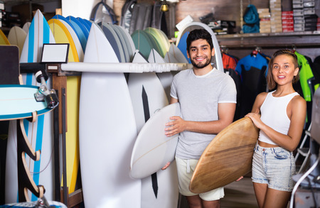 Happy cheerful couple of positive man with boards for surfing in the shopの写真素材