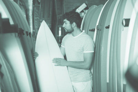 young male surfer holding professional surfboard in the shop for surfingの写真素材