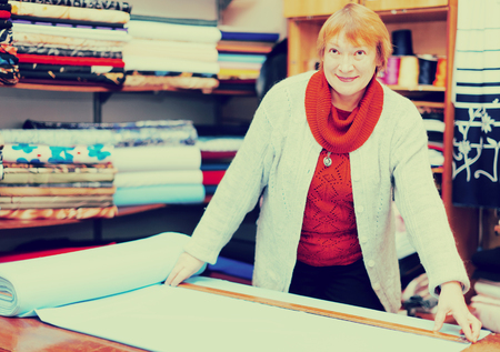 Mature saleswoman measures the fabric in a fabric shopの写真素材