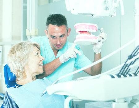 Male dentist explaining future treatment to female patient on dental model