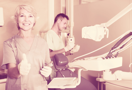 Smiling woman dentist in protective gloves showing thumbs up in the dental clinicの写真素材