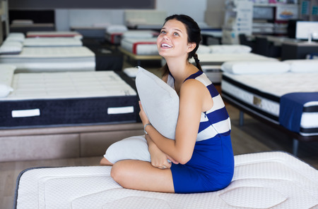 Female is sitting with pillow on mattress in the store.の写真素材