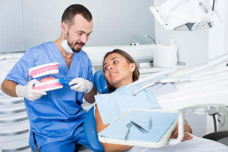Dentist in uniform with maket of jaw is telling about healthcare in dental clinicの写真素材