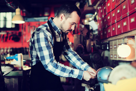 Smiling male worker energetically working on belt buckle in leather workshopの写真素材
