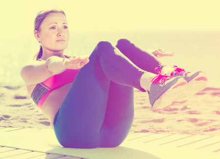 Fitness female stretching muscles on the sand near the seaの写真素材