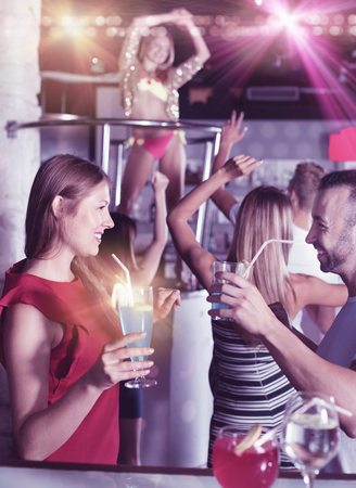 Cheerful positive smiling woman and man joying in the night club with drinks in the handの写真素材
