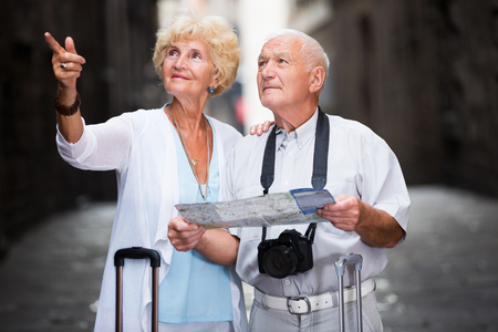 portrait of glad senior travellers with suitcases visiting sights of European city with mapの写真素材