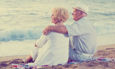 mature man and woman sitting back and hugging on the sea shoreの写真素材