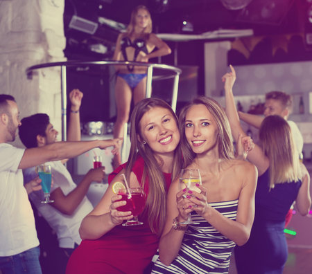 Happy cheerful  females friends with cocktail dancing in the club on party