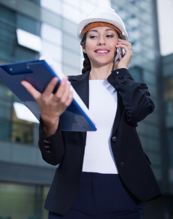 Woman architector in suit and hat is talking about project by the phone near the building.の写真素材