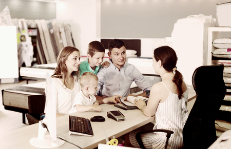 Female assistant in furniture store helping young family in choice of mattress upholsteringの写真素材
