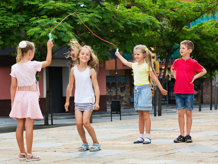 Happy cheerful kids in school age playing together with jumping rope outdoorsの写真素材