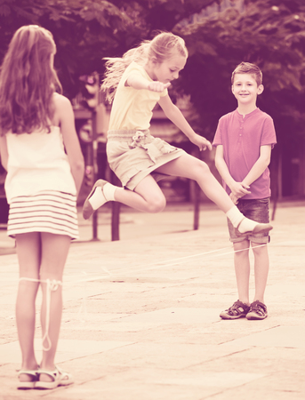 joyful boy and girls in elementary school age jumping over chinese jumping rope at playground . Selective focus on boyの写真素材