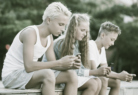 Modern concentrated kids spending time together outdoors using mobile gadgetsの写真素材