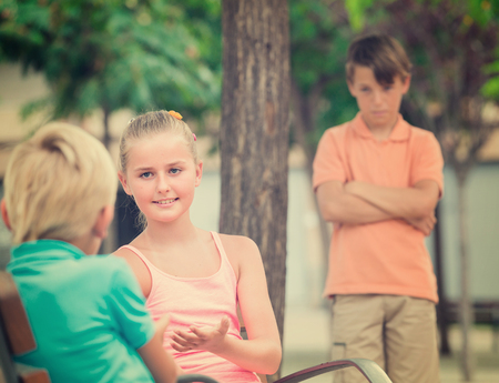 Girl is talking with boy in the distance from their offended friend.の写真素材