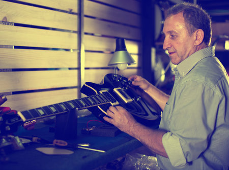 Adult guitarist is repairing his guitar in music studio.