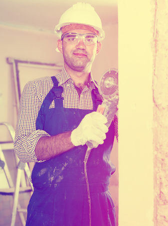 Portrait of smiling repairer man standing with electric saw in uniform indoorsの写真素材
