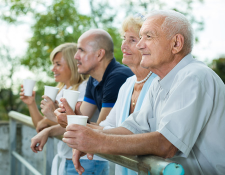 Postive french mature people with plastic cup standing in the parkの写真素材