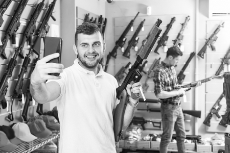 Young man taking selfie with weapon in military shopの写真素材