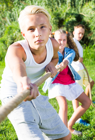 Three happy kids playing active games in summer park, tugging warの写真素材