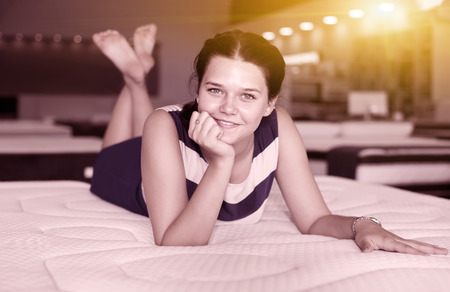 Young woman is lying on bed and posing playfully in the mattress storeの写真素材