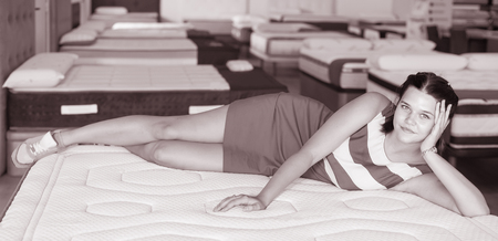 Young french  woman is lying on bed and testing mattress in the store.の写真素材