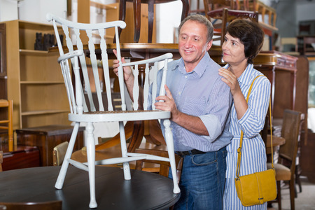 Mature man with his wife are choosing old chair at the antique shop. Focus on both personsの写真素材