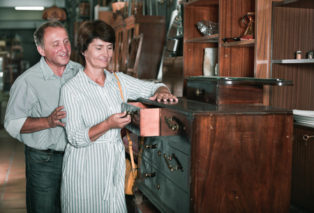 Mature man with his wife are choosing old buffete at antique shop. Focus on both personsの写真素材